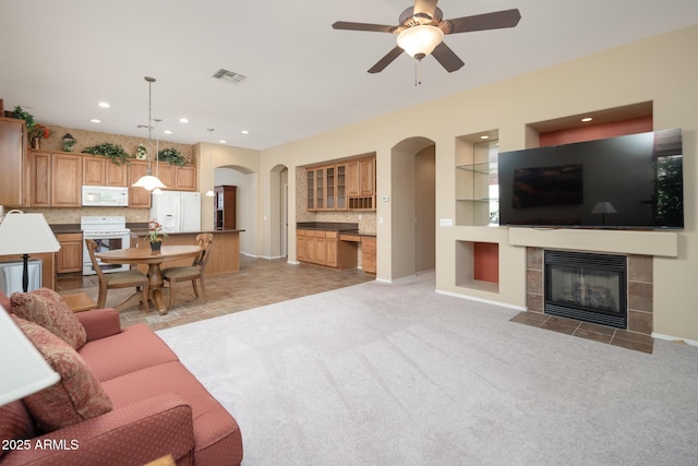 living area with visible vents, baseboards, light carpet, a fireplace, and arched walkways