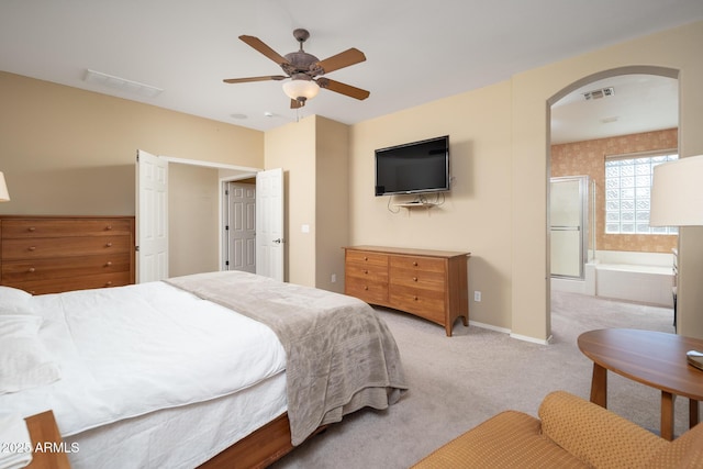 bedroom with baseboards, visible vents, arched walkways, ensuite bathroom, and light carpet