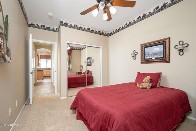 bedroom with a closet, arched walkways, light colored carpet, and baseboards