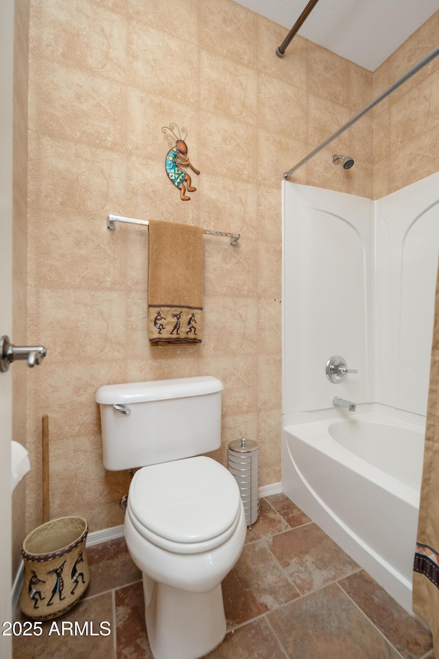 bathroom featuring toilet, baseboards, and shower / washtub combination