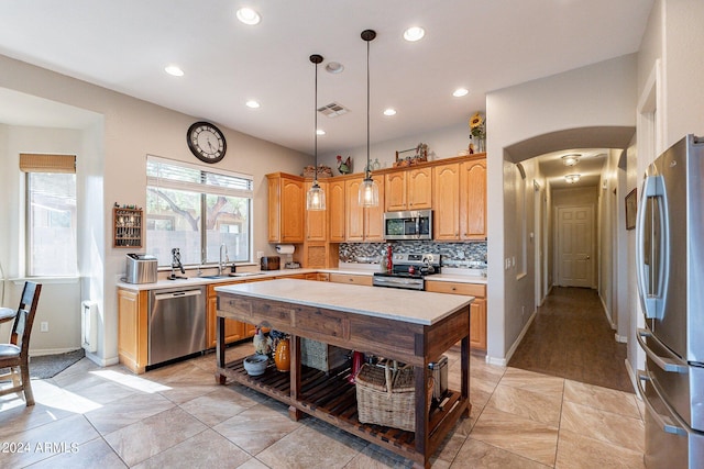 kitchen with a center island, sink, decorative backsplash, appliances with stainless steel finishes, and decorative light fixtures