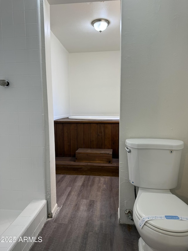 full bath featuring toilet, a tile shower, and wood finished floors