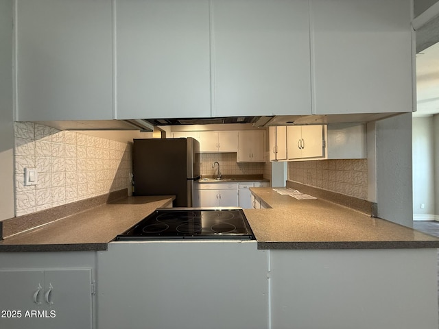 kitchen featuring freestanding refrigerator, backsplash, stovetop, and a sink