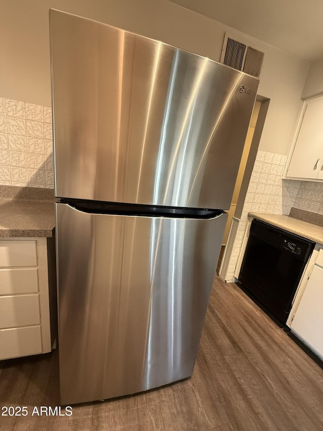 kitchen featuring black dishwasher, freestanding refrigerator, dark wood-type flooring, white cabinetry, and decorative backsplash