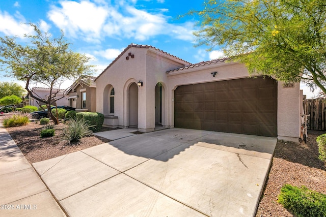 mediterranean / spanish home featuring stucco siding, driveway, a garage, a tiled roof, and fence