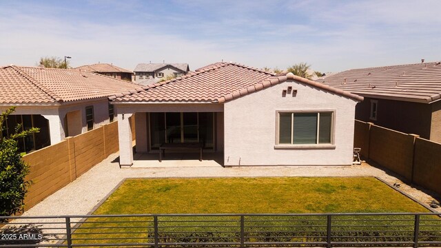 back of property featuring a yard, a fenced backyard, a tiled roof, and stucco siding