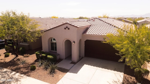 mediterranean / spanish house featuring driveway, a tiled roof, an attached garage, and stucco siding