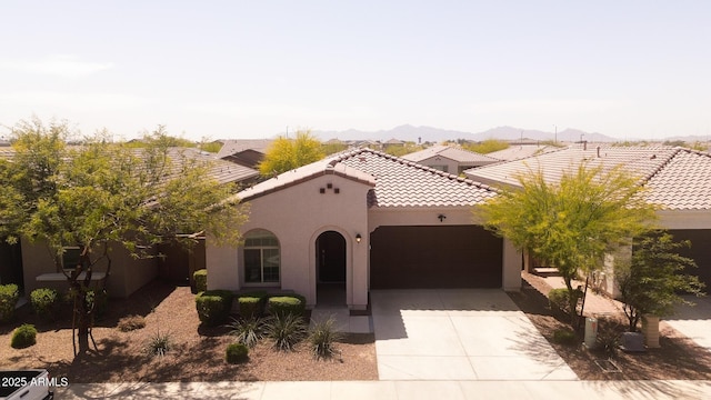 mediterranean / spanish-style home with a mountain view, a tiled roof, an attached garage, stucco siding, and driveway