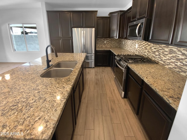 kitchen with appliances with stainless steel finishes, a sink, light stone counters, and tasteful backsplash