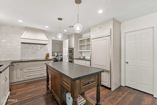 kitchen featuring custom exhaust hood, hanging light fixtures, a kitchen island, dark wood-type flooring, and washer and clothes dryer