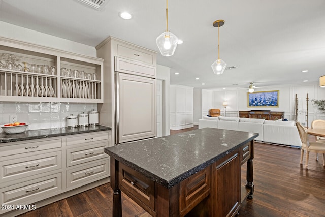 kitchen with dark stone countertops, ceiling fan, dark wood-type flooring, and backsplash