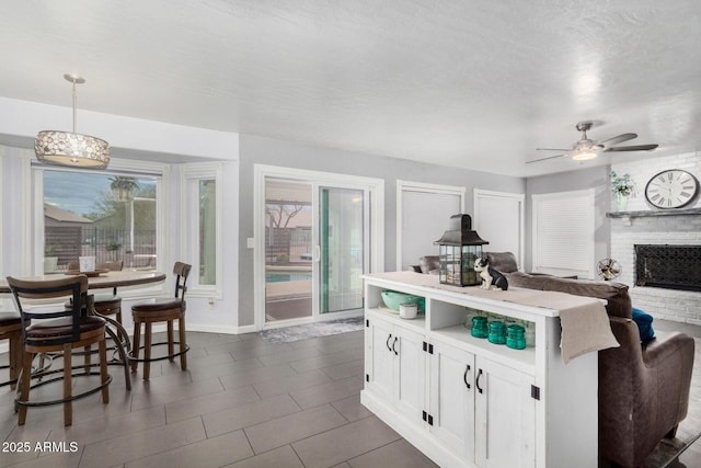 kitchen with pendant lighting, a ceiling fan, a kitchen island, white cabinets, and a brick fireplace