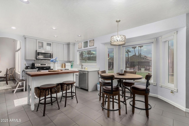 kitchen with backsplash, glass insert cabinets, butcher block counters, appliances with stainless steel finishes, and arched walkways