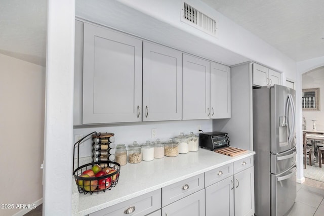 kitchen featuring light tile patterned floors, visible vents, stainless steel fridge, and light countertops