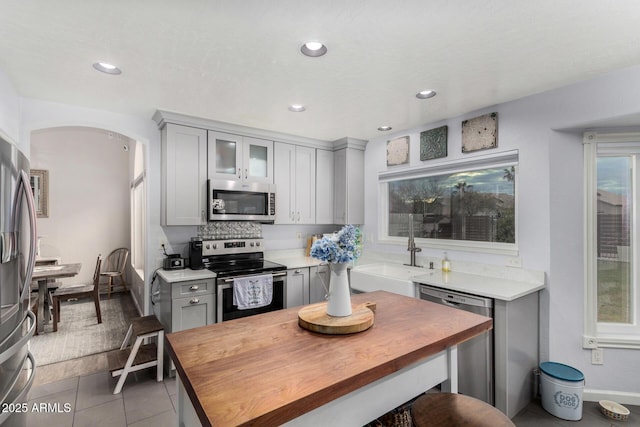 kitchen with a sink, gray cabinetry, wood counters, and stainless steel appliances