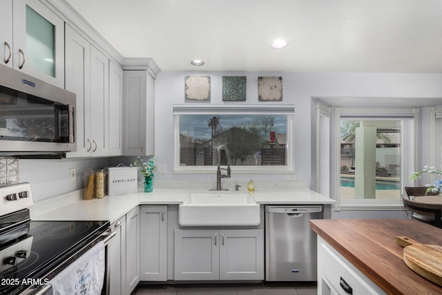 kitchen featuring recessed lighting, gray cabinetry, butcher block countertops, a sink, and appliances with stainless steel finishes