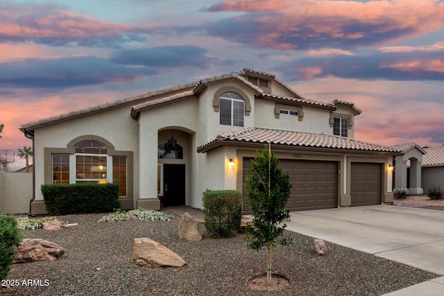 mediterranean / spanish home featuring stucco siding, concrete driveway, an attached garage, and a tiled roof