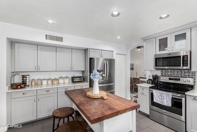 kitchen with light tile patterned floors, visible vents, arched walkways, appliances with stainless steel finishes, and wood counters