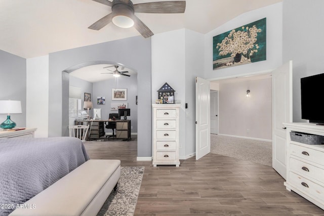 bedroom with vaulted ceiling, wood finished floors, arched walkways, and baseboards