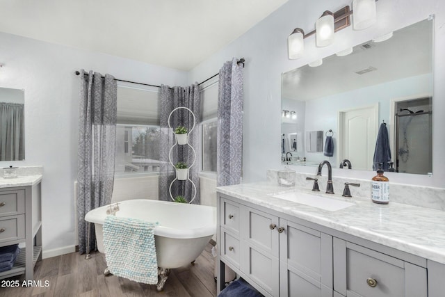 bathroom with a freestanding tub, visible vents, two vanities, a sink, and wood finished floors