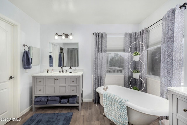 full bath featuring vanity, a freestanding tub, wood finished floors, and baseboards