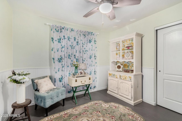 sitting room with a wainscoted wall and a ceiling fan