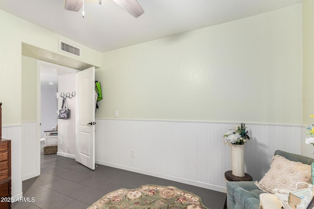 living area with visible vents, a ceiling fan, and a wainscoted wall