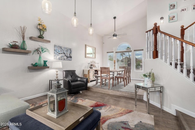 living room featuring high vaulted ceiling, wood finished floors, stairway, baseboards, and ceiling fan