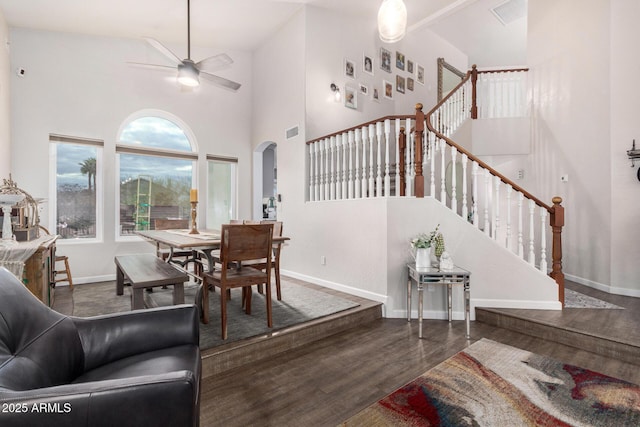 dining space with baseboards, ceiling fan, stairway, a towering ceiling, and wood finished floors