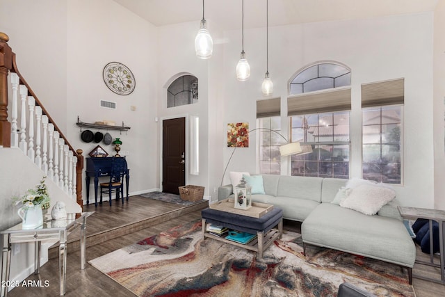 living area featuring visible vents, baseboards, stairs, a high ceiling, and wood finished floors