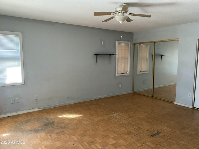 unfurnished bedroom featuring ceiling fan, a textured ceiling, baseboards, and two closets