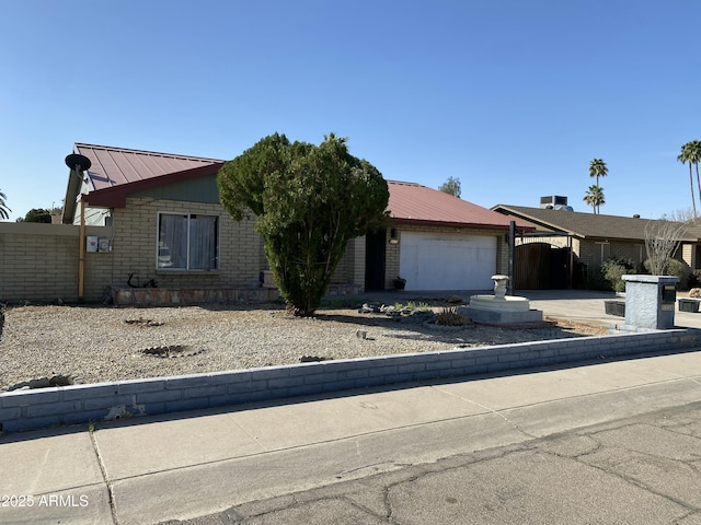 view of front of home with metal roof, concrete driveway, brick siding, and fence