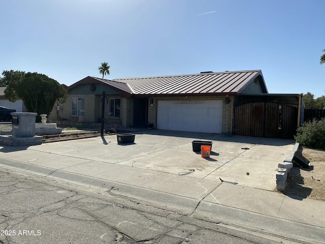 ranch-style home with concrete driveway, metal roof, an attached garage, a standing seam roof, and brick siding