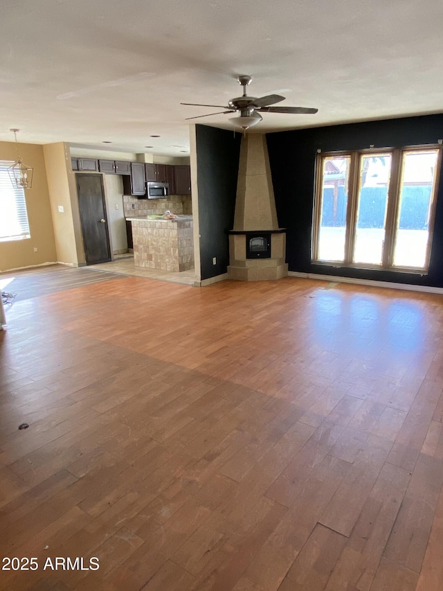 unfurnished living room with light wood-style floors, baseboards, and ceiling fan with notable chandelier