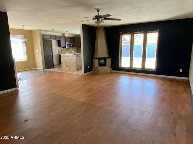 unfurnished living room featuring ceiling fan with notable chandelier, light wood-style flooring, and baseboards