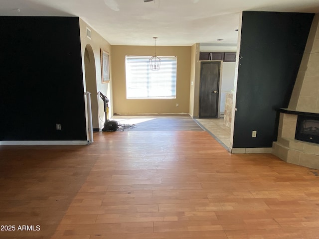 unfurnished living room with arched walkways, a tile fireplace, visible vents, baseboards, and light wood finished floors