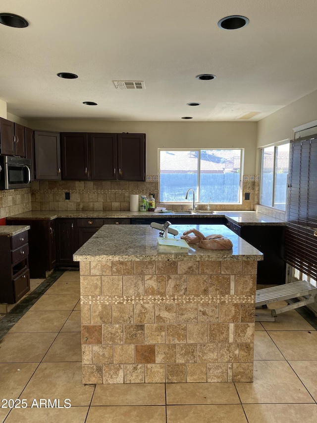 kitchen with stainless steel microwave, light tile patterned flooring, visible vents, and light stone countertops