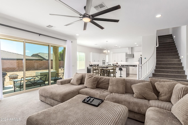 carpeted living room with ceiling fan with notable chandelier