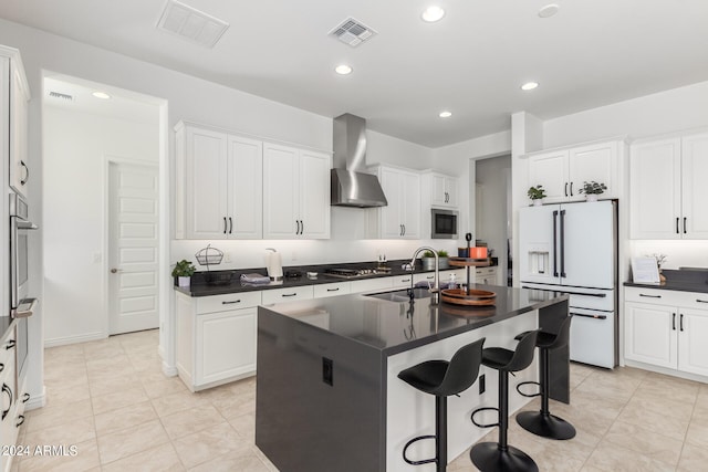 kitchen featuring wall chimney exhaust hood, white cabinets, a center island with sink, and white fridge with ice dispenser