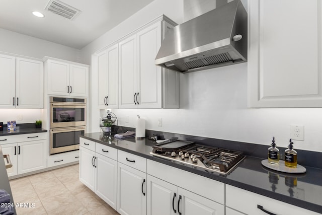 kitchen with white cabinetry, wall chimney range hood, stainless steel appliances, and light tile patterned flooring