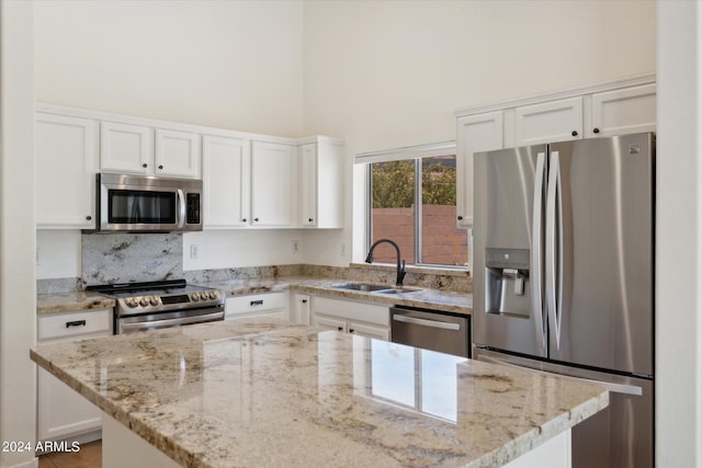 kitchen featuring white cabinetry, sink, a center island, light stone counters, and appliances with stainless steel finishes