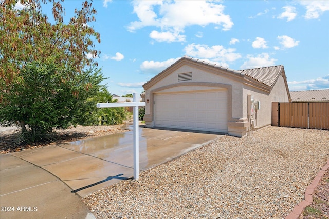 exterior space with driveway, a tiled roof, an attached garage, fence, and stucco siding