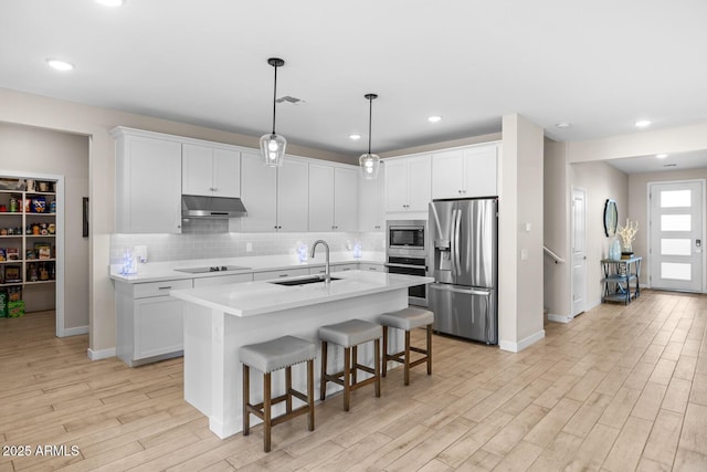 kitchen with a sink, stainless steel appliances, under cabinet range hood, light wood-type flooring, and light countertops