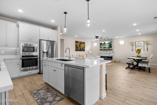 kitchen featuring a sink, stainless steel appliances, open floor plan, a ceiling fan, and a stone fireplace