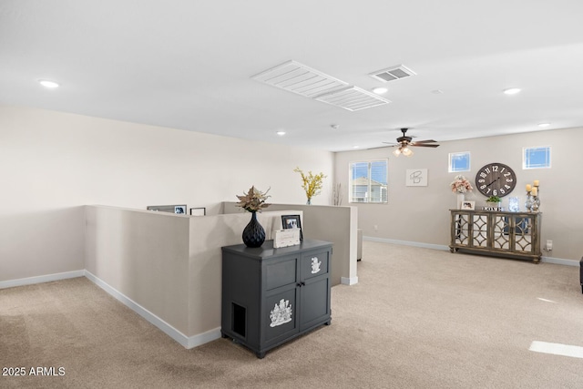 hall with an upstairs landing, visible vents, baseboards, and light carpet
