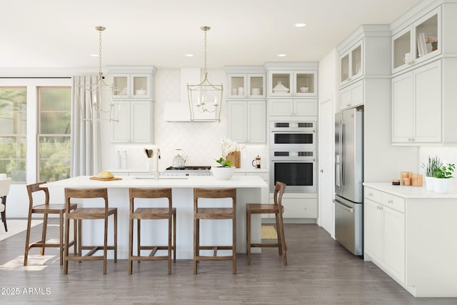 kitchen with double wall oven, stainless steel refrigerator with ice dispenser, white cabinets, hanging light fixtures, and a kitchen island with sink