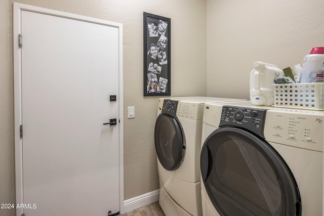 clothes washing area featuring laundry area, washing machine and clothes dryer, light wood finished floors, a textured wall, and baseboards