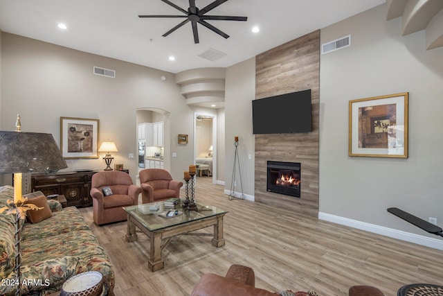 living area featuring a tile fireplace, light wood-style floors, a ceiling fan, visible vents, and arched walkways