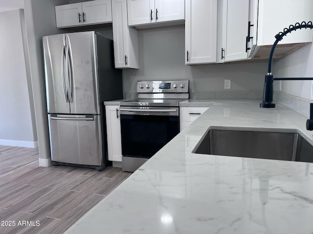 kitchen featuring light wood finished floors, light stone counters, baseboards, white cabinets, and appliances with stainless steel finishes