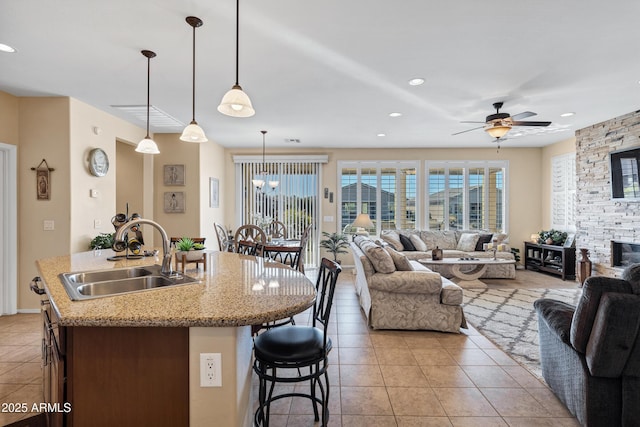 kitchen featuring sink, light tile patterned floors, ceiling fan, hanging light fixtures, and a center island with sink